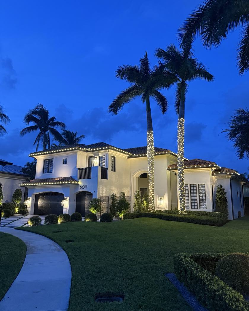 Home lit warm white with tall wrapped palms against a purple sky